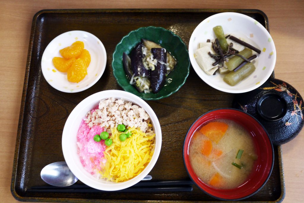 きょうのお昼ごはんは、3色丼・炊き合わせ・蒸しナスの薬味がけ・根菜汁・くだものでした。