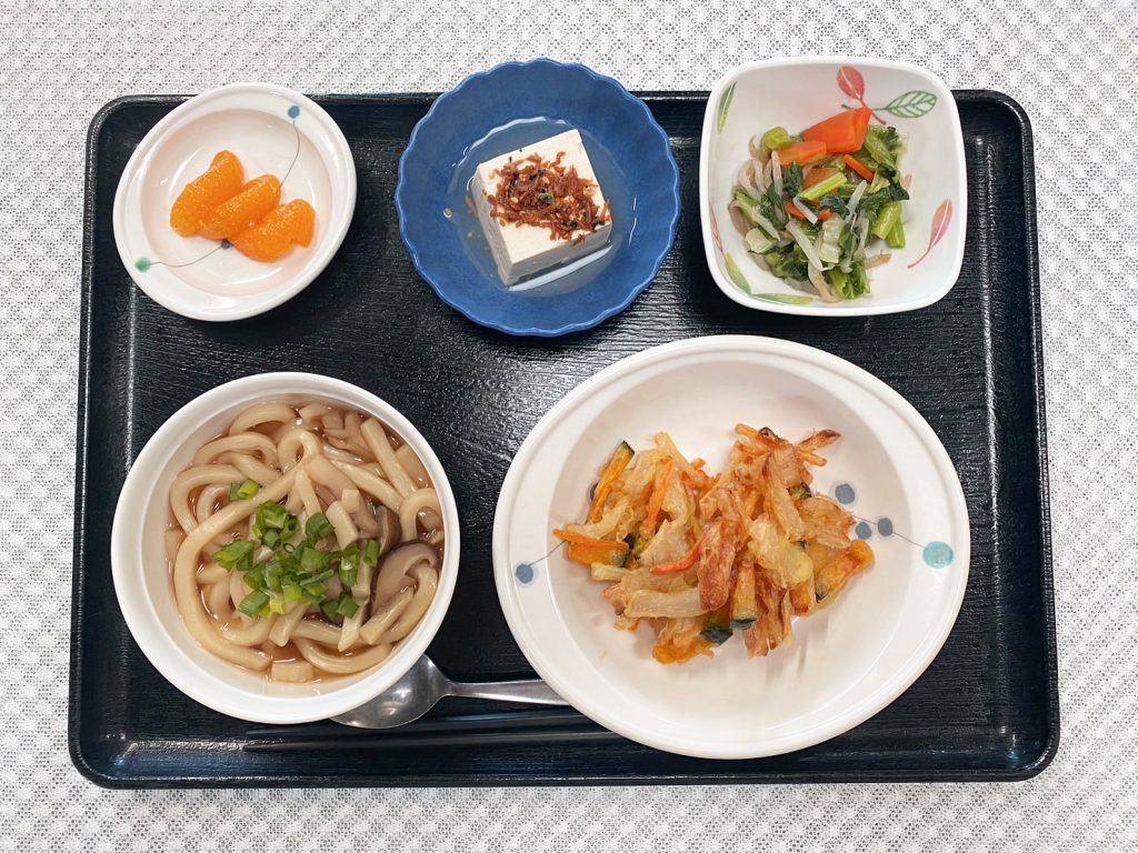 12月14日水曜日　きょうのお昼ごはんは、きのこうどん・かき揚げ・青菜和え・煮奴・くだものでした。